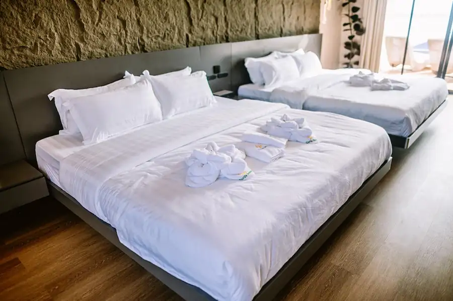 Two large beds decorated with turtle towel art against a textured stone wall inside the Family Deluxe room at Turtle Seaweed Resort.